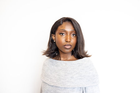 Portrait of a young woman with straight hair, wearing a stylish off-shoulder sweater against a white background.の写真素材