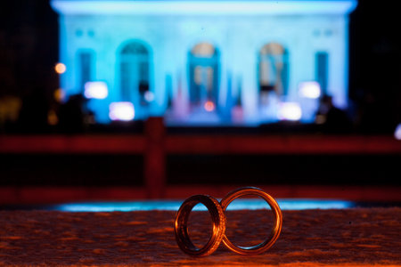 Two wedding rings in focus with a beautifully lit architectural building in the background at night.の写真素材