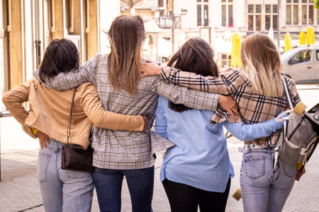 Four friends with arms around each other walking outdoors, showcasing friendship and casual fashion.の写真素材