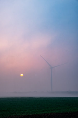 A wind turbine silhouette is pictured against a misty sunrise, illustrating clean energy in a peaceful environmentの写真素材