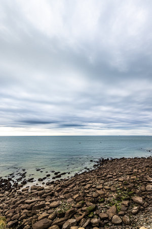 The seascape portrays a rocky shoreline under a cloudy sky, with tranquil waters, creating a serene coastal sceneの写真素材