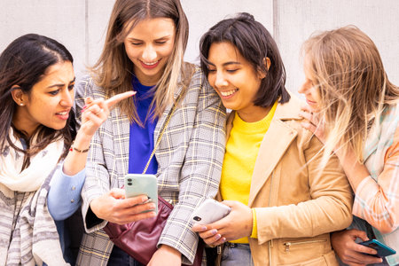 A joyful moment is shared by four young women who are smiling and laughing together, looking at...