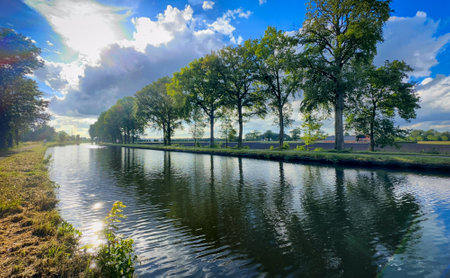 A serene canal scene adorned with lush green trees, beautifully reflecting the tranquility of natures splendorの写真素材