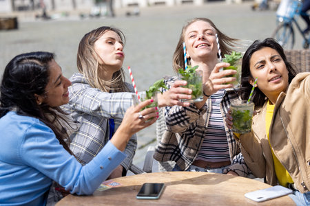 Four women having fun together outdoors, drinking mojitos and capturing moments on a lively sunny day.の写真素材