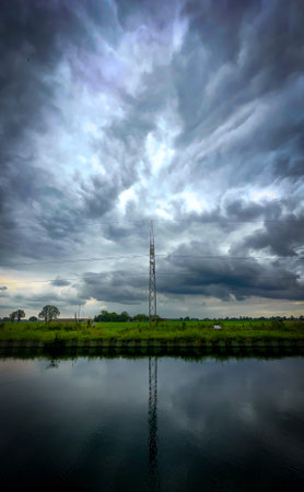A striking view of a tall tower set against a stormy sky, beautifully reflected in the calm water belowの写真素材