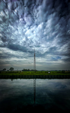 A striking and captivating view of a tall tower beautifully reflected in the tranquil waters beneath a moody skyの写真素材