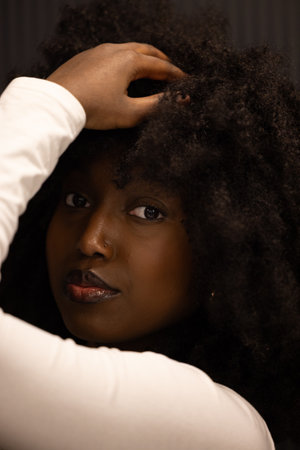 A closeup portrait of a woman with voluminous curly hair in a white sweater, looking contemplative and elegantの写真素材
