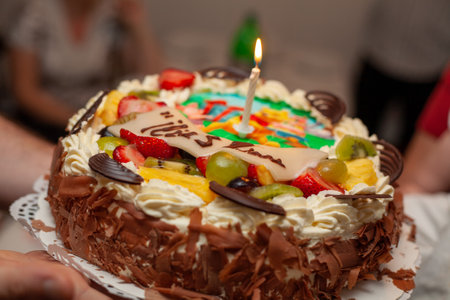 A colorful birthday cake topped with fresh fruits and a lit candle, perfect for joyful celebrationsの写真素材