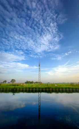 A picturesque landscape showcases a tall tower beautifully reflected in the calm waters beneath a stunning skyの写真素材