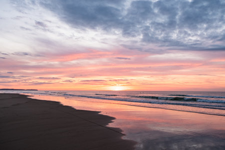 Beautiful sunrise over a serene beach scene with colorful sky and calm ocean waves reflecting sunlight.の写真素材