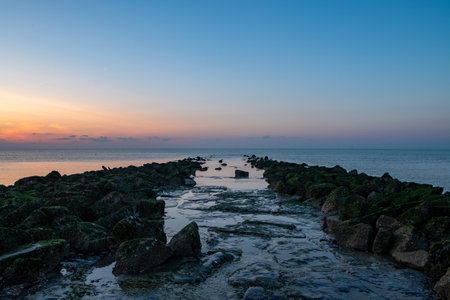 A stunningly breathtaking view of a rocky jetty during a vibrant sunset, creating a beautifully tranquil coastal sceneの写真素材