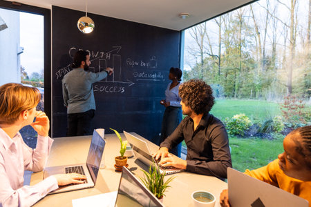 Multicultural team working together in a meeting room, brainstorming ideas on blackboards, using laptops.の写真素材