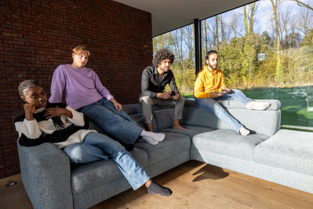 Four friends lounging on a sofa in a bright, modern living room with large windows and natural light.の写真素材