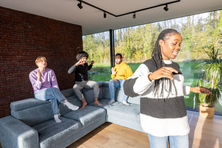 Group of diverse friends having fun and playing video games together in a modern living room with large windows.の写真素材