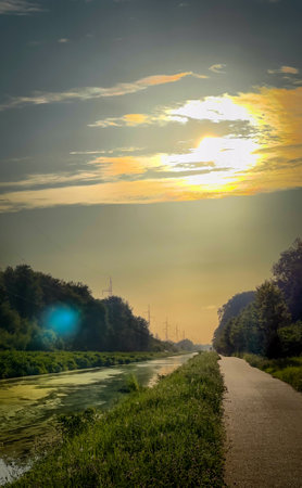 The breathtaking and picturesque view of a tranquil pathway runs alongside a calm and reflective waterway during sunsetの写真素材