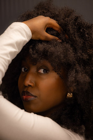 Close-up portrait of a woman with a voluminous curly afro hairstyle holding her head with a confident look.の写真素材