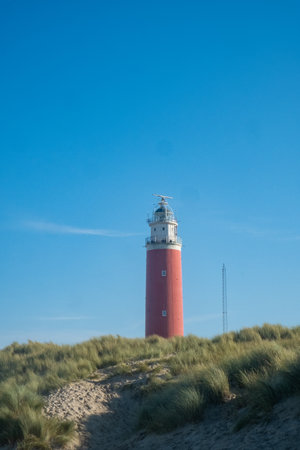 Eierland, De Cocksdorp, Texel, The Netherlands, Oktober 28th, 2024, A vibrant and colorful lighthouse stands tall and proud amidst the lush green dunes, all under a bright blue skyの写真素材