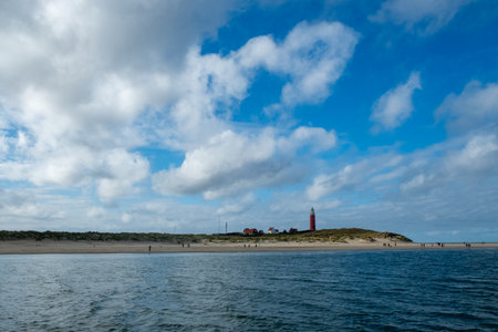 Eierland, De Cocksdorp, Texel, The Netherlands, Oktober 28th, 2024, A truly captivating seaside view showcasing a historic lighthouse set against a dramatic, vibrant sky and calm watersの写真素材