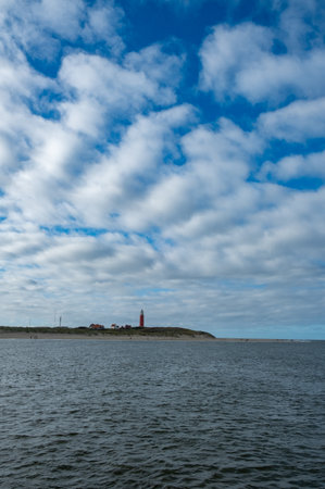 Eierland, De Cocksdorp, Texel, The Netherlands, Oktober 28th, 2024, A picturesque view of a lighthouse on a distant shore under a stunning sky filled with fluffy cloudsの写真素材
