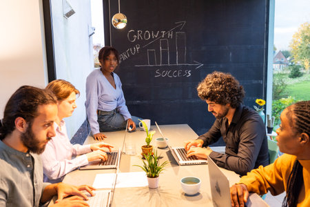 Diverse team collaborating with laptops in a modern office, brainstorming growth and success strategies.の写真素材