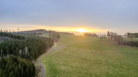 A breathtaking sunset beautifully illuminating the vast green fields and the dense forests surrounding itの写真素材
