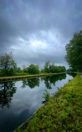 A tranquil river scene with lush greenery along the banks and beautiful clouds reflecting in the calm waterの写真素材