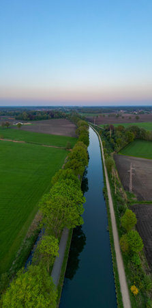 Sint Jozef, Rijkevorsel, Antwerp, Belgium, 27th of April, 2025, An aerial shot captures a peaceful river meandering through green fields at sunset, creating a picturesque sceneの写真素材
