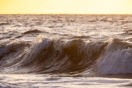 Experience the breathtaking beauty of ocean waves illuminated by a stunning golden sunset on the distant horizonの写真素材