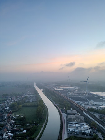 Lot, Beersel, Vlaams-Brabant, 22nd of April, 2025, A stunning aerial shot of a calm river, lush fields, and wind turbines under a beautiful pastel skyの写真素材