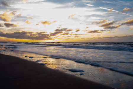 A beautiful sunset reflects on gentle waves at the tranquil beach, capturing natures enchanting beautyの写真素材