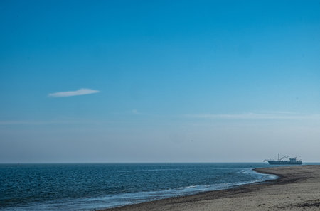 Eierland, De Cocksdorp, Texel, The Netherlands, Oktober 28th, 2024, A serene view of a peaceful shoreline landscape showcasing calm waters along with a distant vessel upon a pristine skyの写真素材