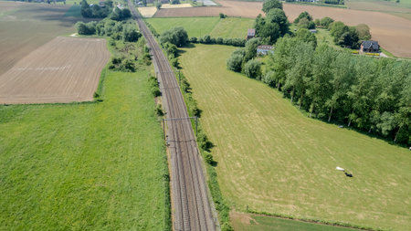 A breathtaking aerial view showcases railway tracks elegantly weaving through vibrant fields and lush greeneryの写真素材
