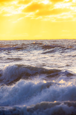 A breathtakingly serene view of the gentle ocean waves as they crash softly beneath a warm, golden sunset skyの写真素材