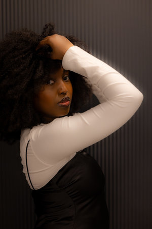 Portrait of a confident woman with curly hair, posing in stylish black and white outfit against a dark background.の写真素材