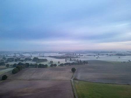A tranquil aerial perspective of a misty farmland landscape beautifully illuminated under a serene dawn skyの写真素材