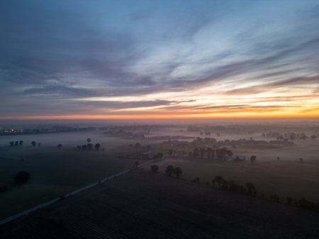 Witness a stunning aerial view of a breathtaking sunrise, casting vibrant colors over the foggy fields belowの写真素材