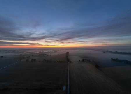 A breathtaking view of a stunning sunrise beautifully illuminating the misty fields, showcasing natures pure beautyの写真素材