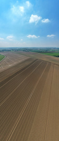 Expansive farmland with freshly plowed soil, vividly showcasing agricultural patterns alongside vibrant greeneryの写真素材