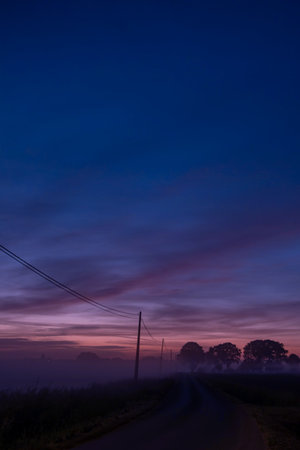A peaceful and serene morning scene showcasing a winding road set against the backdrop of colorful dawn skiesの写真素材