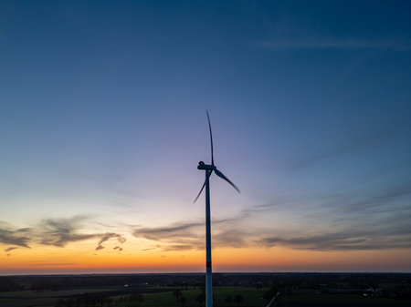 Experience a breathtakingly beautiful view of a wind turbine dramatically silhouetted against a colorful sunset skyの写真素材