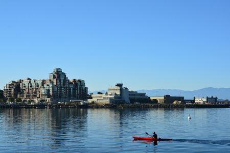 A kayaker paddles his way past high end real estate as he heads to the inner harbor in Victoria BCのeditorial素材