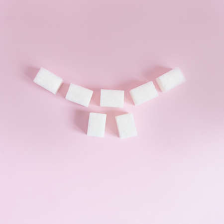 cubes of white sugar are laid out in the form of a smile with teeth on a pink background