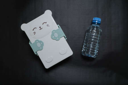 closed lunch box with a cute muzzle and a bottle of water on a black background.の写真素材