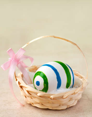 Painted easter egg in a basket with ribbonの写真素材