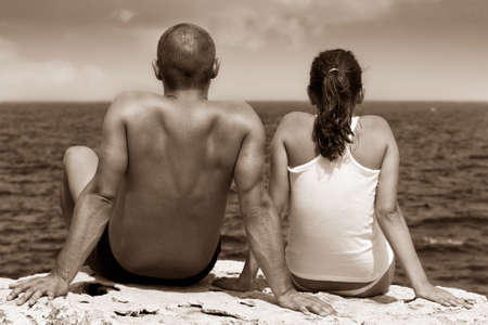 Young couple sitting on a cliff and looking at seaの写真素材