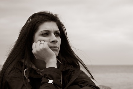 B&W portrait of attractive young woman feeling moody and sitting by the sea or oceanの写真素材