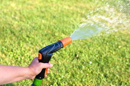 Female hand watering the grass with a garden hose with sprinklerの写真素材