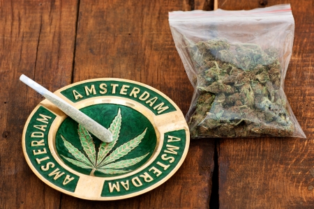 Marijuana Joint in an ashtray with amsterdam sign  and a big plastic bag of weed on wooden backgroundの写真素材