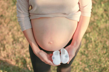 Closeup photo of pregnant woman  holding baby shoesの写真素材