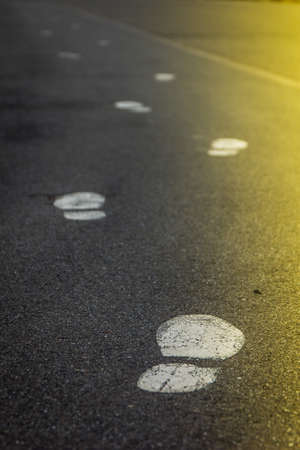 Footsteps marks on asphalt. Vertical and sunlit from right